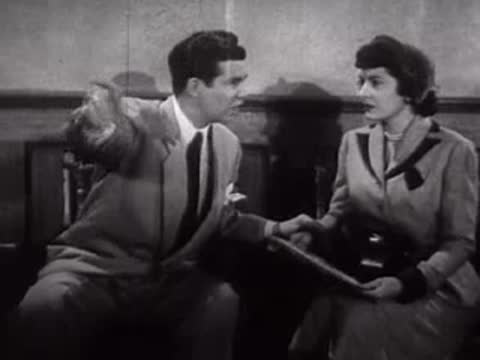 A man points enthusiastically while sitting next to a woman reading a paper.