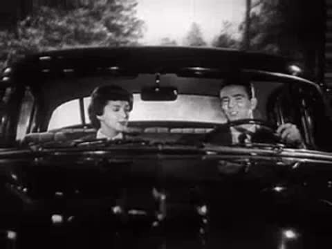 Man and woman in a parked car talking, viewed from the front.