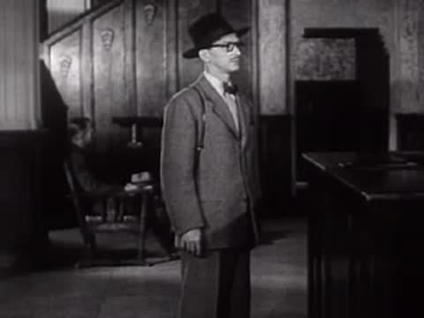 A soldier stands at attention inside a public room, mid-century.