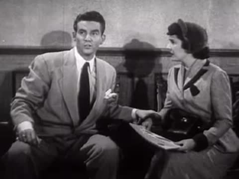 A man and woman sit together talking in a waiting room, mid-century.