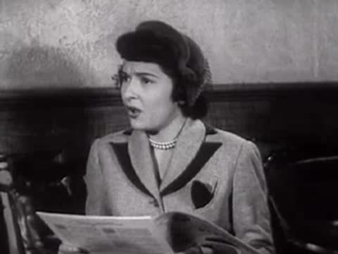 A woman reading a newspaper while sitting inside a building.
