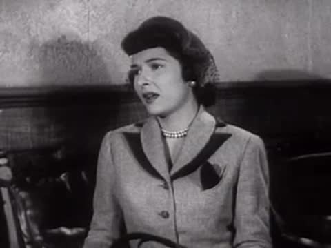 A woman sitting indoors and looking around.