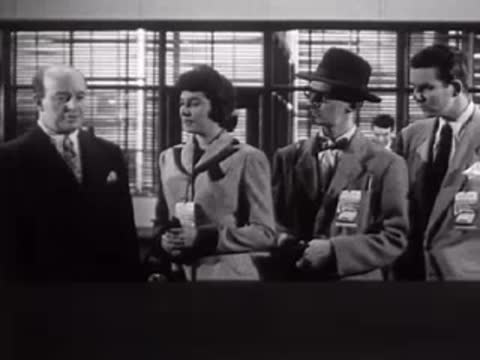 A group of people standing and talking indoors near windows.
