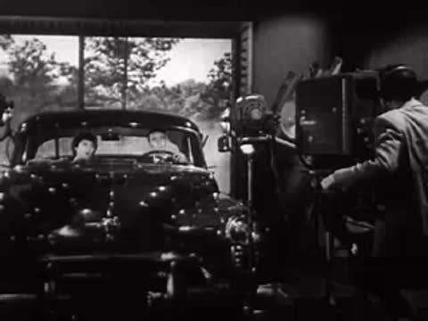 Car on a soundstage with a camera crew recording the scene.