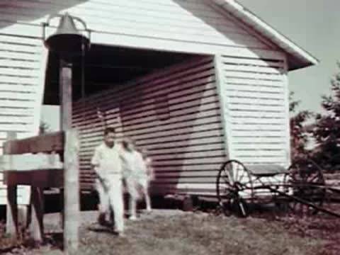 Children running towards a large white barn with open doors on a farm.
