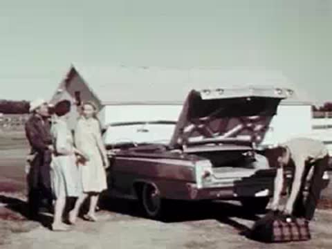 People loading luggage into the open trunk of a classic convertible car.