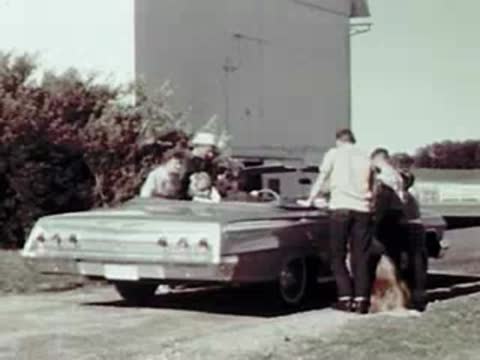 People getting into a convertible parked outside a building on a farm.