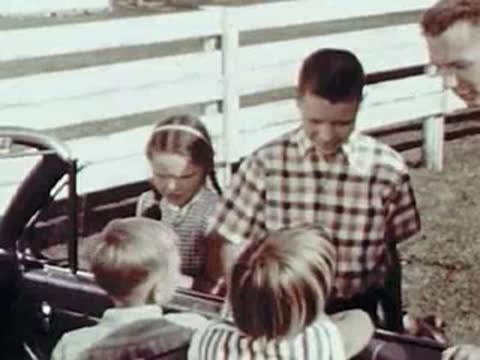 Children standing by a fence talking to people inside a parked convertible car.