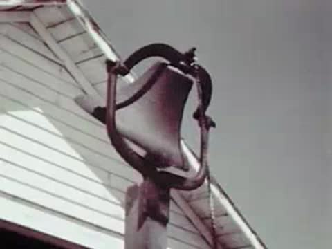 Close-up view of a large metal farm bell swinging and ringing.