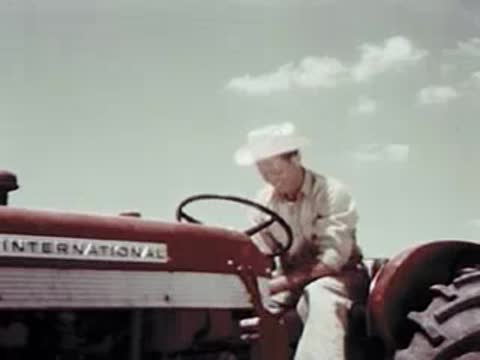 A man sitting on a red tractor pointing and getting off the vehicle.