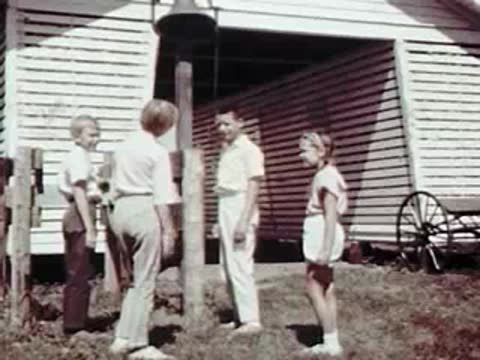 Children standing near a fence and walking towards a barn.
