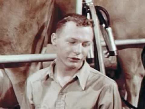A man talking inside a dairy barn near milking equipment.