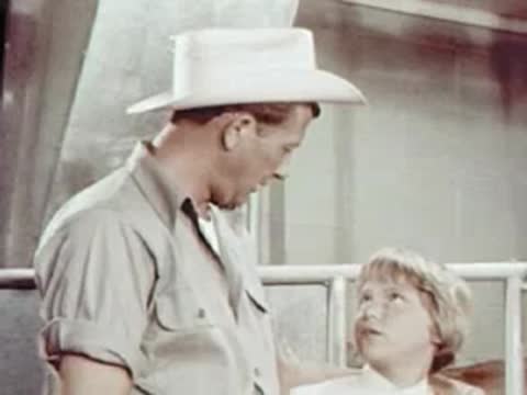 A man in a cowboy hat talking to a child in a dairy barn.