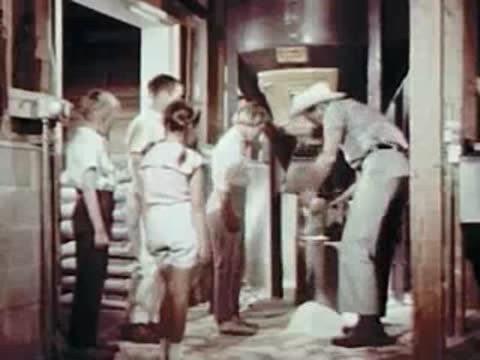 Man demonstrating feed to children in a barn