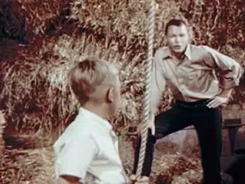 Boy and man talking in a hayloft near a rope