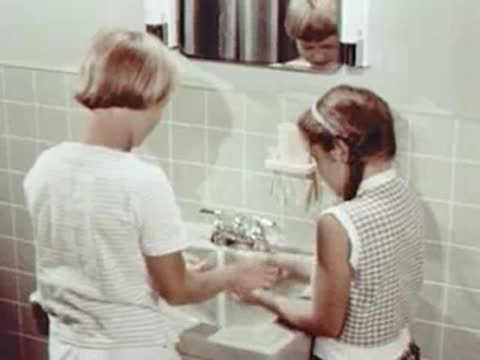 Two children washing their hands at a bathroom sink.