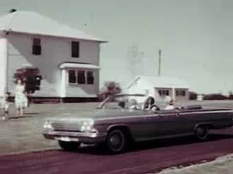 A car driving up to a large white farmhouse and barn on a farm.