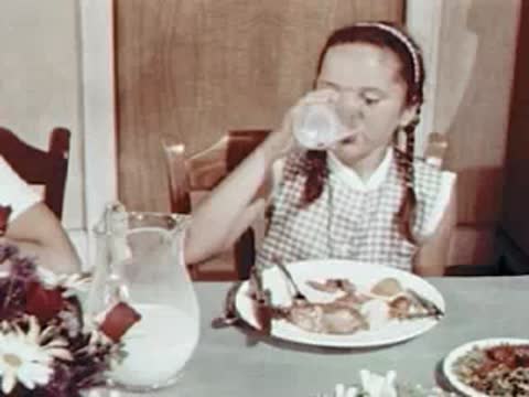 Child drinking milk from a glass at the dinner table.