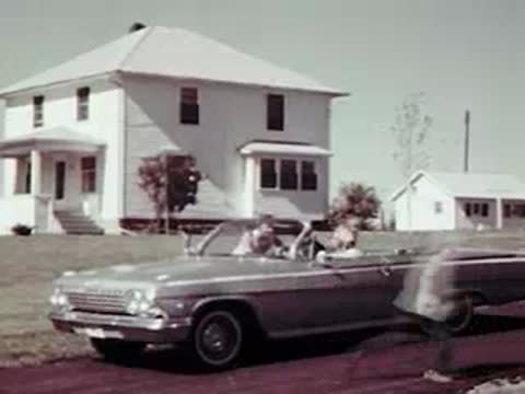 Children getting out of a parked convertible in front of a farmhouse.