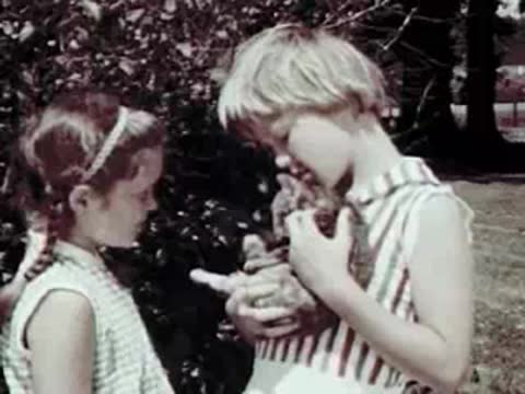 Two young girls holding small animals outdoors near bushes