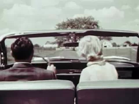 A tracking shot from inside a convertible looking at the driver and passenger.