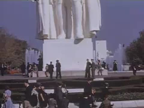 Pan right across a statue group on a high pedestal surrounded by strolling visitors.