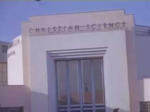 Pan right across the facade of the Christian Science building with visitors walking below.