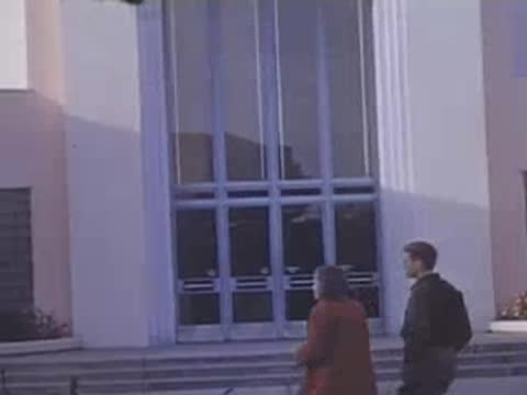 Pan right following visitors walking up steps toward the entrance of an exposition hall.