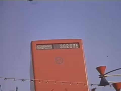 Pan right past a large red sign displaying numbers against a clear blue sky.
