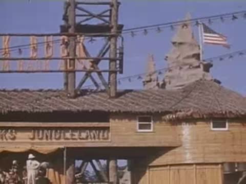 Pan right across the entrance sign for Frank Buck's Jungleland attraction with American flags.