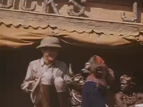Safari performer interacts with a chimpanzee wearing striped clothing near a drum performance.