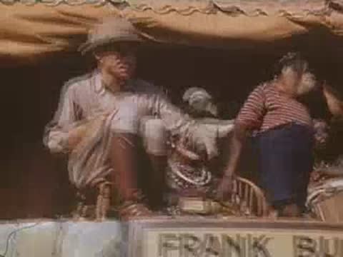 A chimpanzee in striped shirt and trousers interacts with a safari guide on a stage.