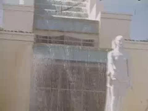 A medium shot of a white statue of a woman near a cascading water feature.