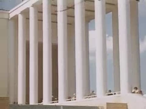 A medium shot of the ITALIA pavilion colonnade with people walking nearby.