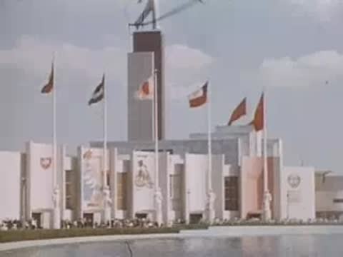A wide shot of a large pavilion with multiple flags flying against a cloudy sky.