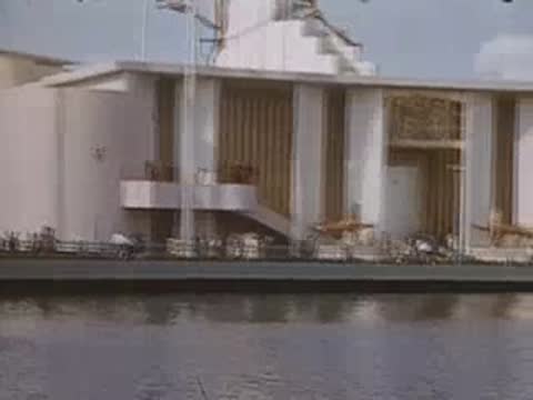 A medium shot of a modern pavilion exterior by a body of water with flags.
