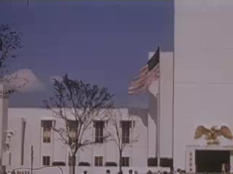 Panning shot of the exterior of the United States building with American flags flying.