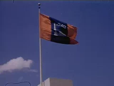 Low angle medium shot of a large flag flying on a tall pole against a blue sky.