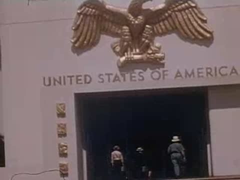 Medium close-up of the entrance of the United States building with an eagle emblem.