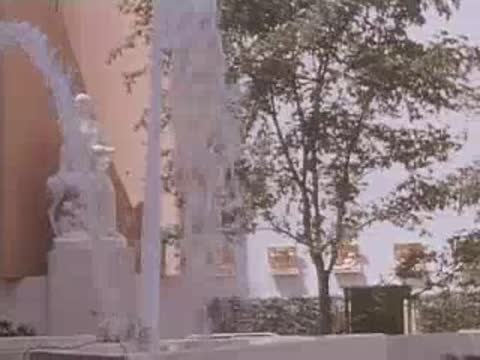 Medium shot of water fountains spraying in front of a building facade and statues.