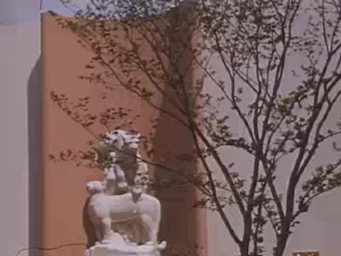 Medium shot of a white animal sculpture against a curved wall and bare trees.