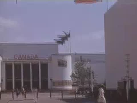 Wide shot of the Canada pavilion building with national flags and people walking outside.
