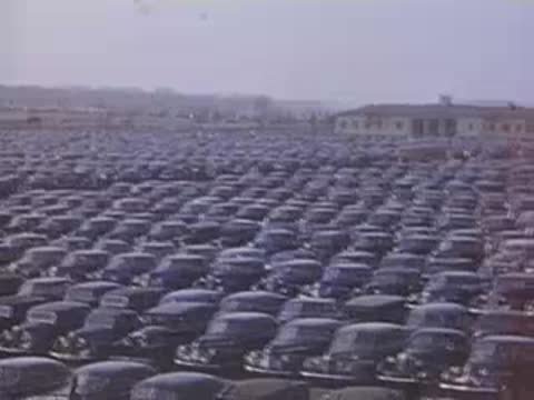 Aerial wide shot looking down over a massive parking lot packed with vintage cars.