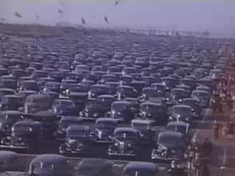 Wide shot panning across the enormous parking lot filled with rows of classic cars.