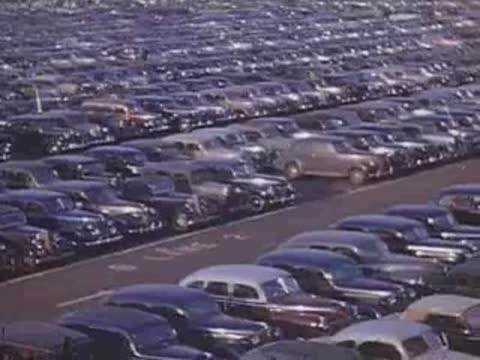 Wide shot panning over a crowded parking lot with rows of parked cars.