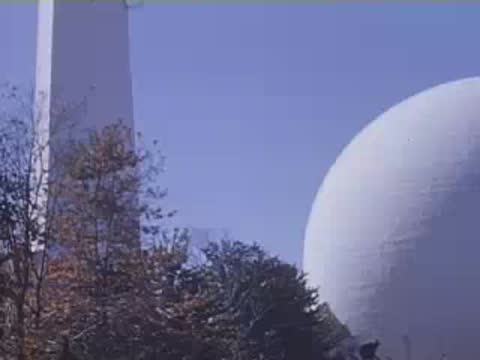 Panning upwards along the towering white triangular Trylon obelisk next to the large spherical Perisphere.
