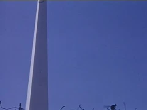 A sharp upward angle focusing on the very tall, tapering white Trylon obelisk against a blue sky.