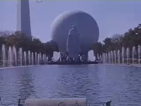 A large statue standing in front of the Perisphere with fountains spraying across a reflecting pool.