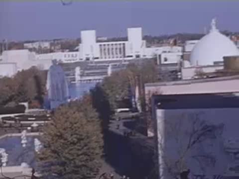 An elevated panoramic view showing a large statue, exhibition halls, and a domed building amid trees.