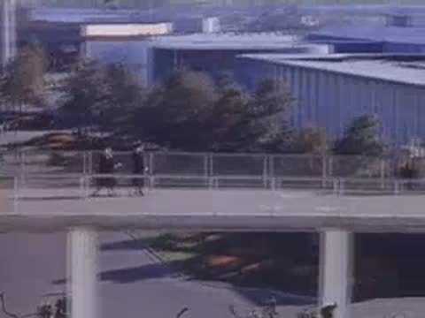 Visitors walking across an elevated pedestrian bridge with white railings between exhibition areas.